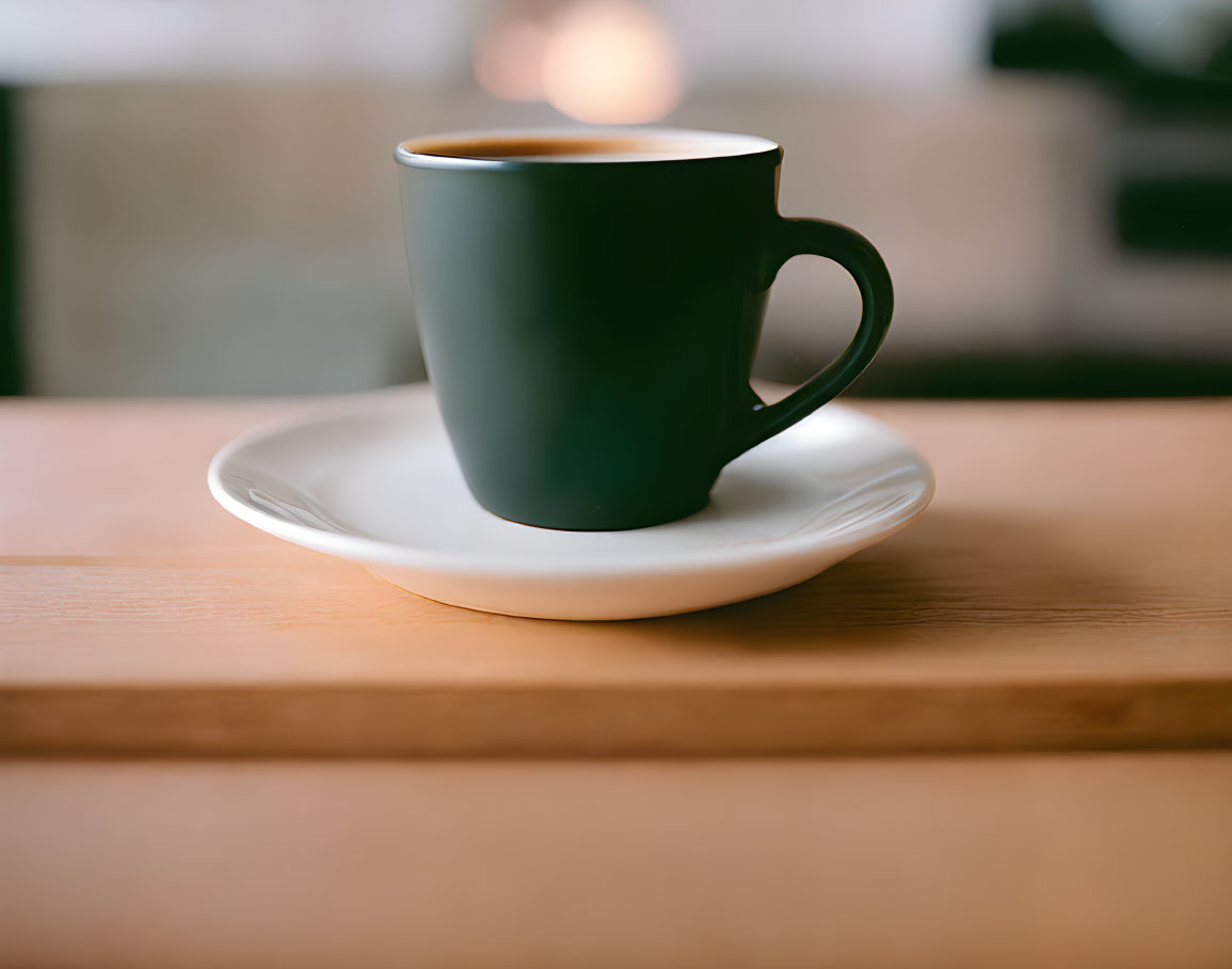 Green mug with hot beverage on white saucer on wooden surface