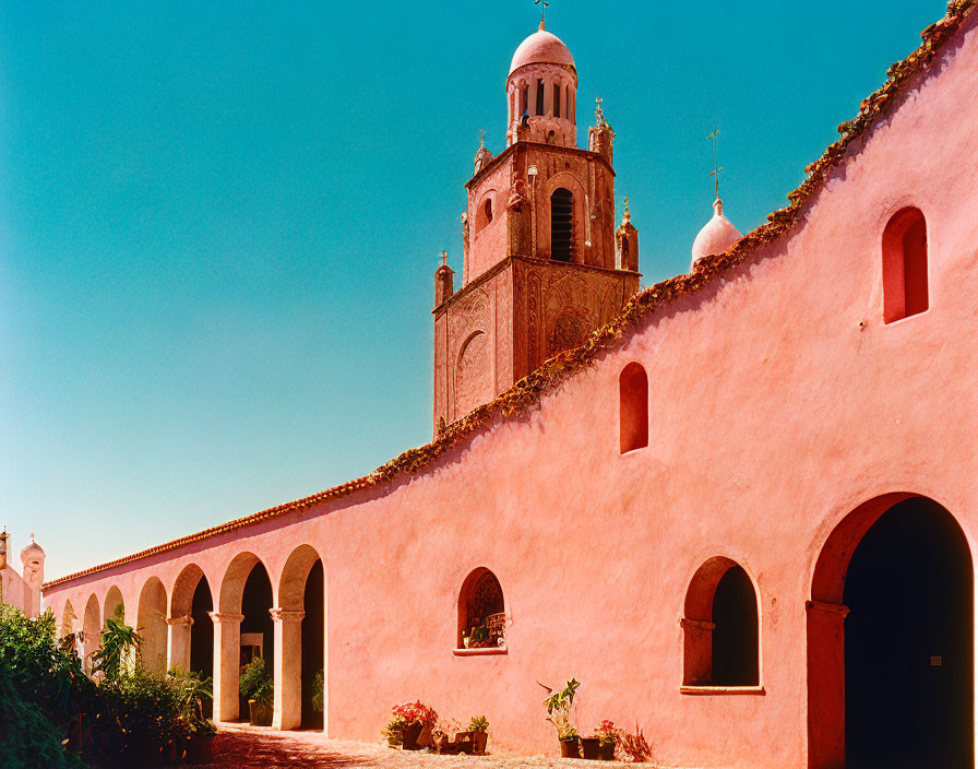 Pink-walled building with archways and bell tower under blue sky