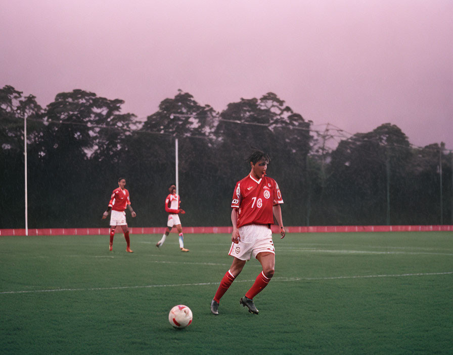 Soccer players on rainy pitch, one player dribbling ball