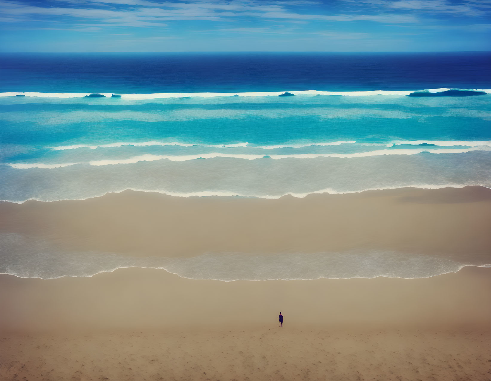 Person walking on sandy beach with blue ocean and cloudy sky