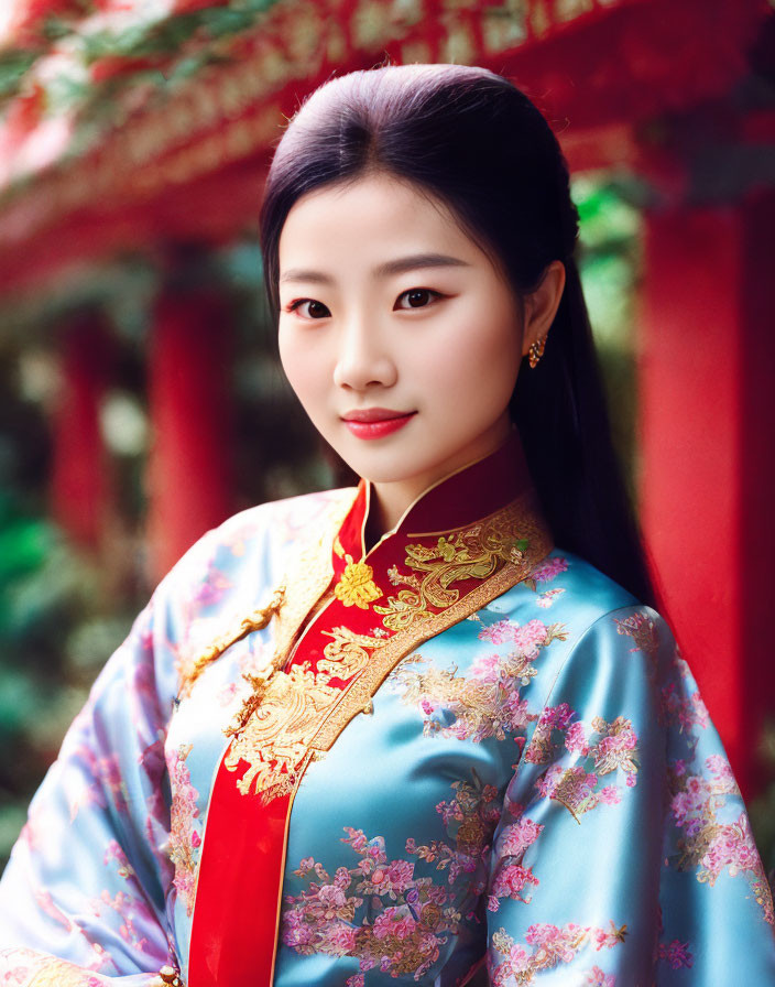 Young woman in blue and red Asian dress with gold embroidery in front of red structure.