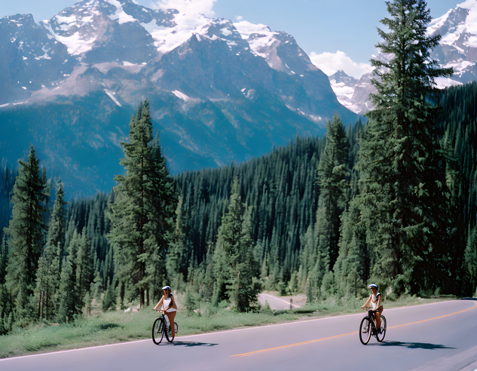 Cyclists on mountain road with snow-capped peaks