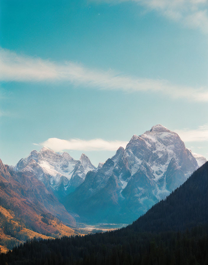 Snow-capped mountains under clear blue sky with green foothills