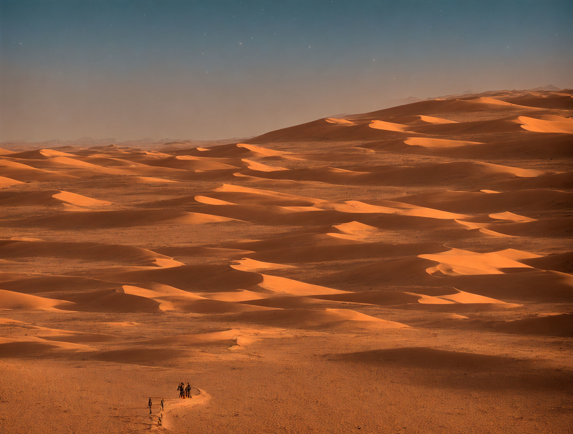 Group of people crossing vast sand dunes under hazy sky