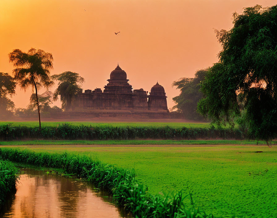 Tranquil landscape: Historical temple silhouettes, lush greenery, water body, warm orange