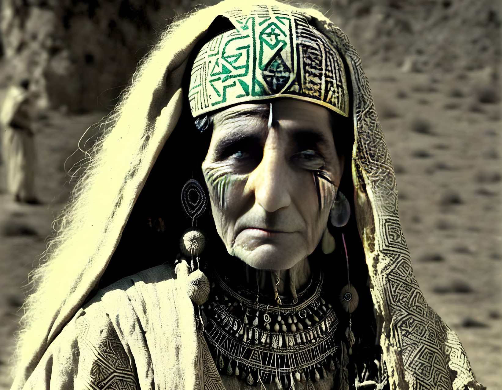 Elderly person in traditional attire with jewelry and facial tattoos against barren backdrop