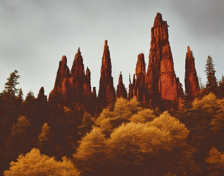 Towering red rock spires over golden forest under overcast sky