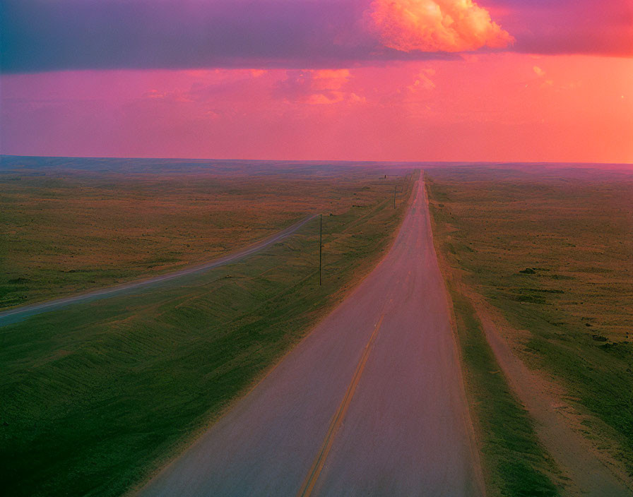 Straight road under vibrant purple and pink sky in flat landscape