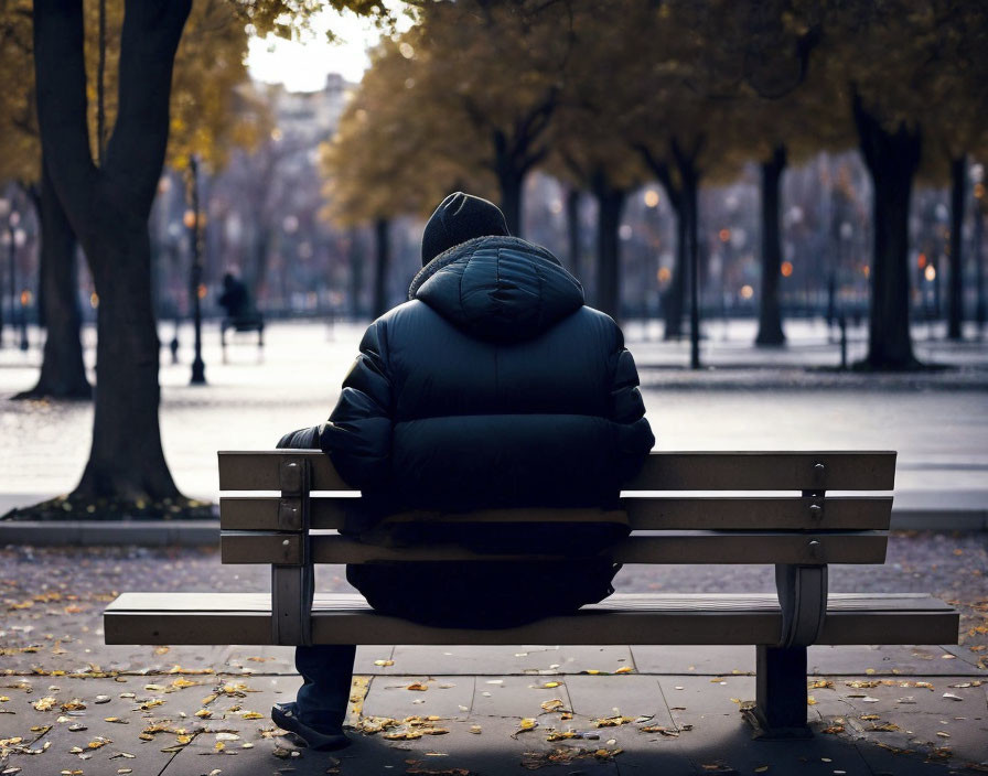 Lonely figure on park bench at dusk among autumn trees.