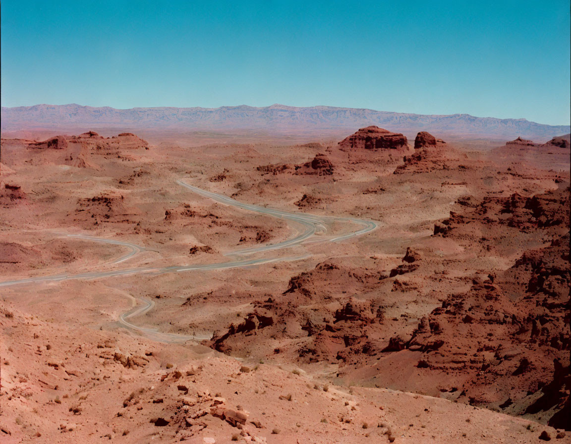 Sinuous desert road amid rocky terrain under clear blue sky