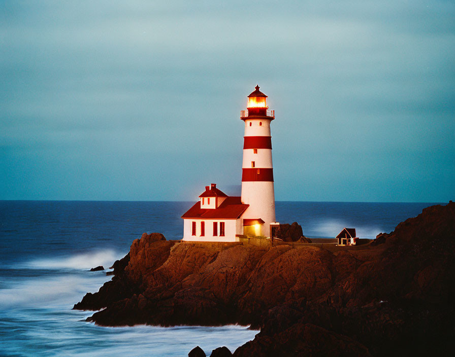 Red and White Striped Lighthouse on Rocky Coastline at Twilight