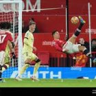 Red football player leaps high for header in match with red-clad spectators.