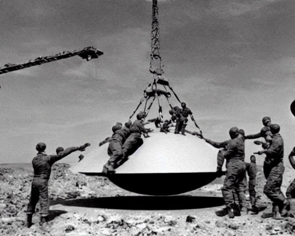 Military men lift UFO-like object with crane in desert.