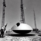 Military men lift UFO-like object with crane in desert.