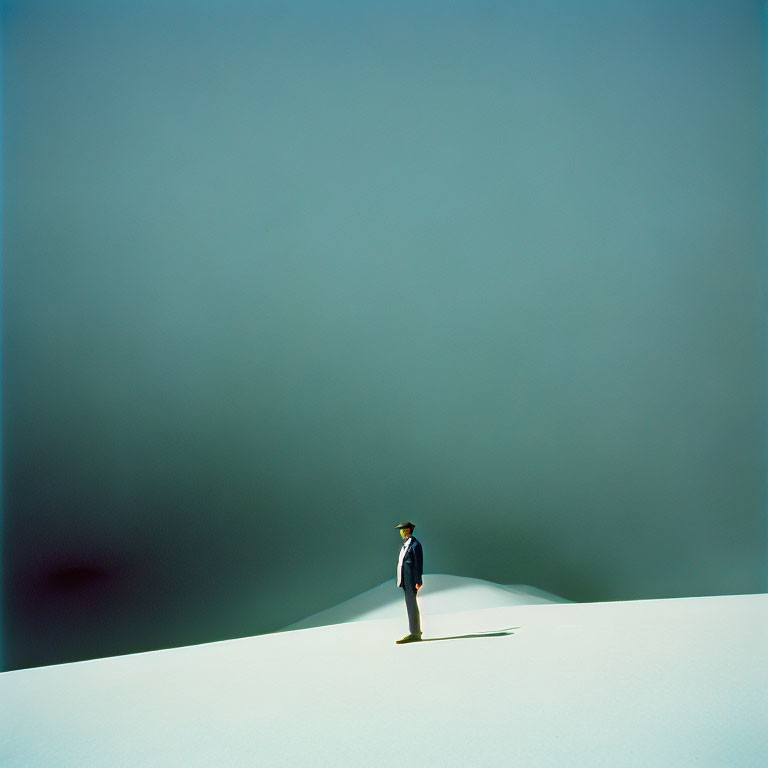 Person in suit and hat on dune under gradient sky symbolizes solitude