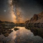 Tranquil landscape with starry sky, towering rocks, calm river, lush greenery, purple