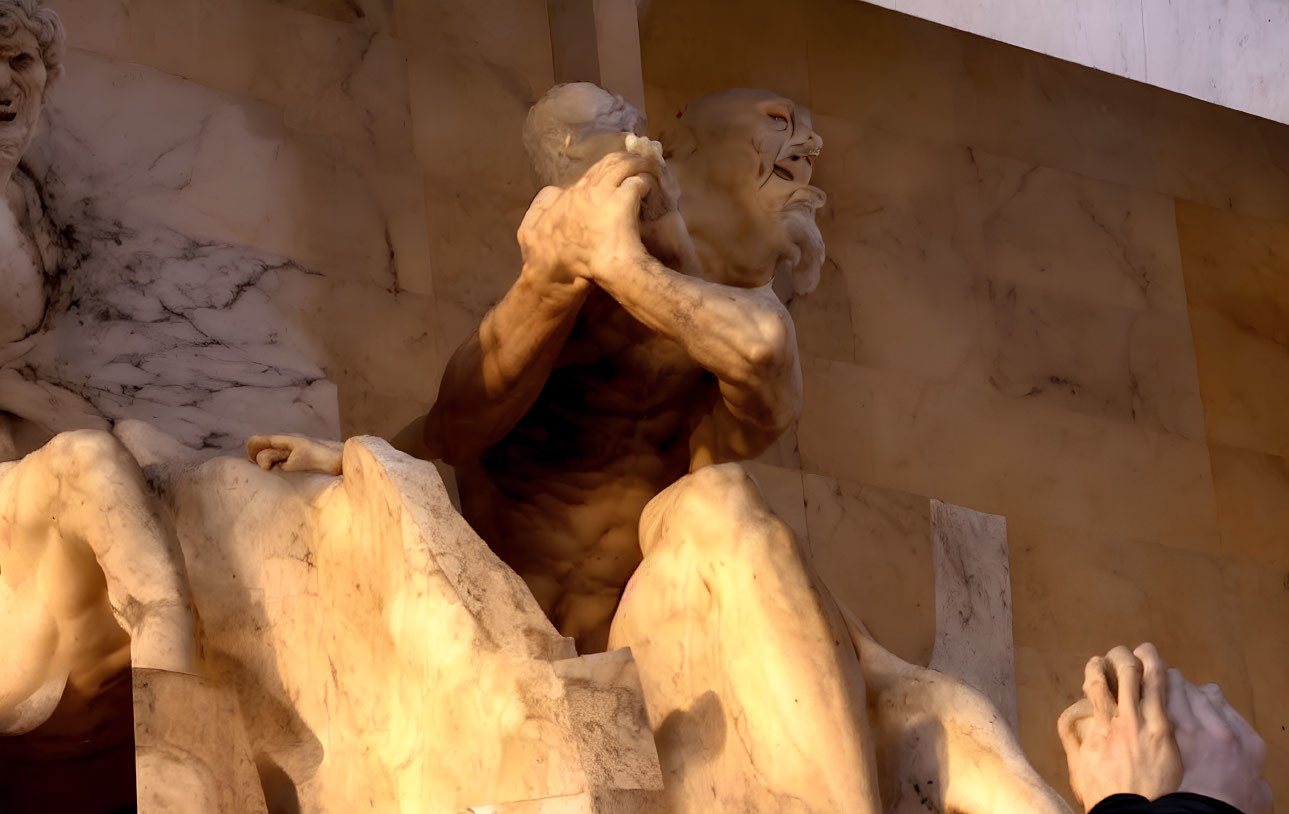 Muscular male figure holding up another against warm-colored stone