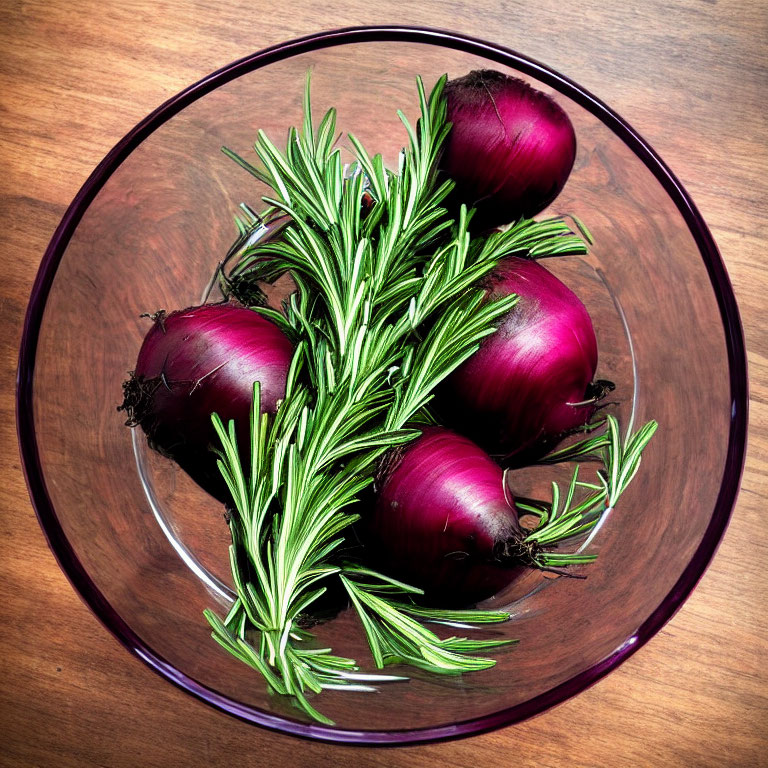 Glass bowl with red onions and rosemary on wooden surface