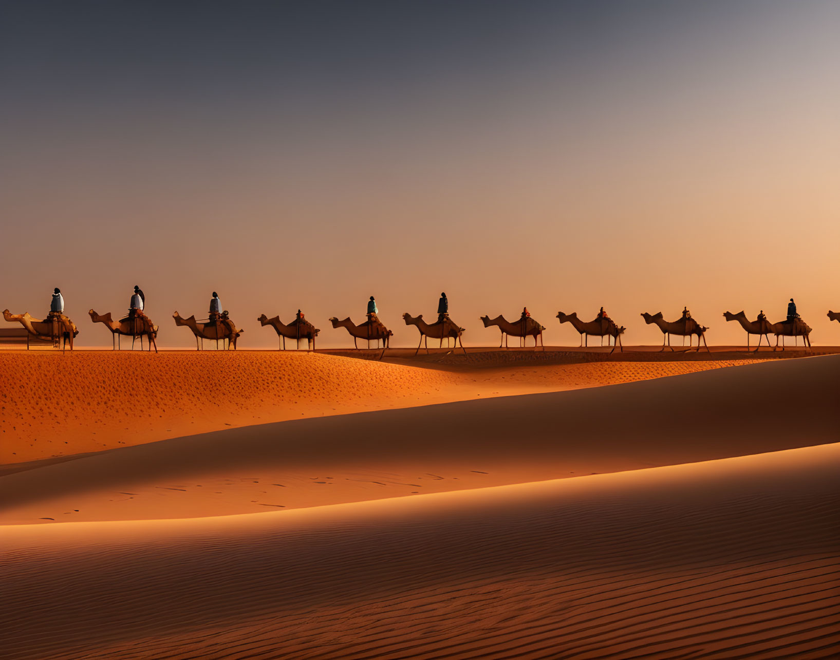 Camel caravan and riders crossing sunlit desert dune