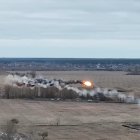 Helicopter flying over rural area with explosions and smoke.