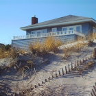 Ocean-view beachfront house with blue and white exterior and sandy surroundings.