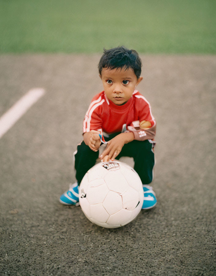 Child in red sports kit with whistle on soccer field.