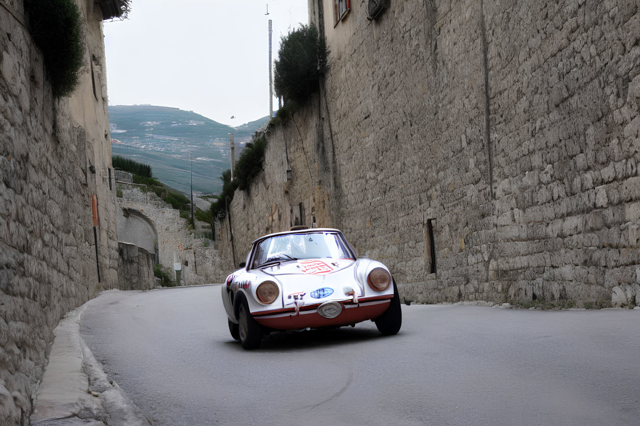 Vintage Race Car on Cobblestone Street with Stone Walls and Hills