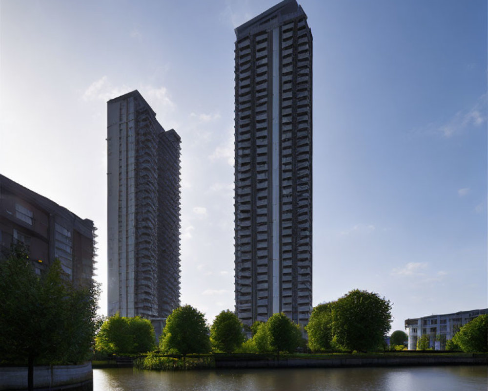 Tall residential skyscrapers by calm water and greenery at dusk