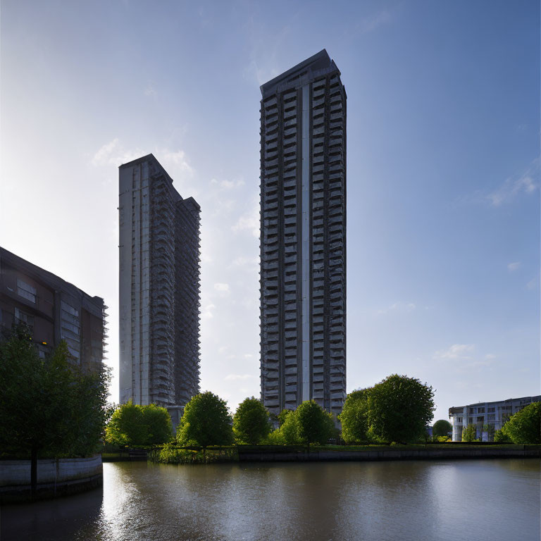 Tall residential skyscrapers by calm water and greenery at dusk