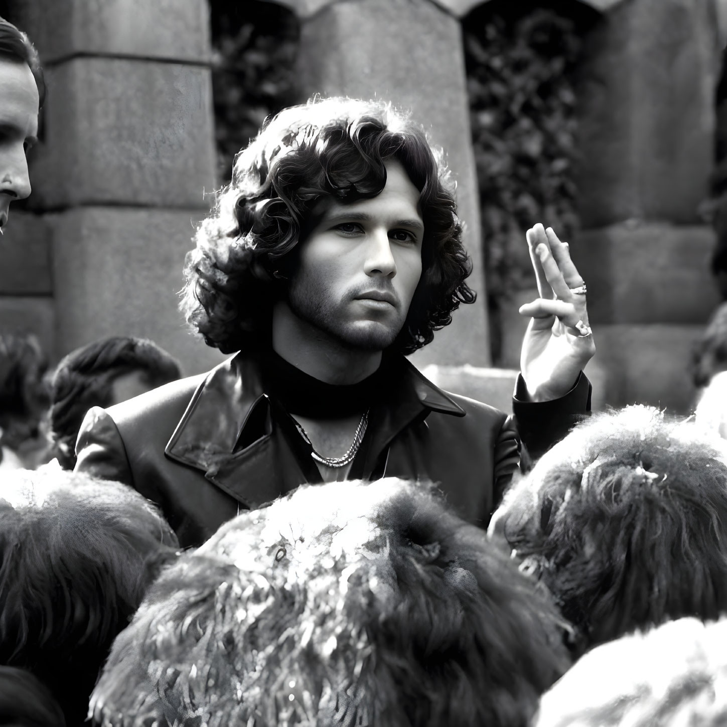 Monochrome curly-haired man in leather jacket with raised hand among crowd