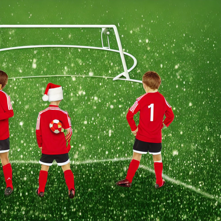 Children in red soccer uniforms on snowy green pitch with Santa hat.