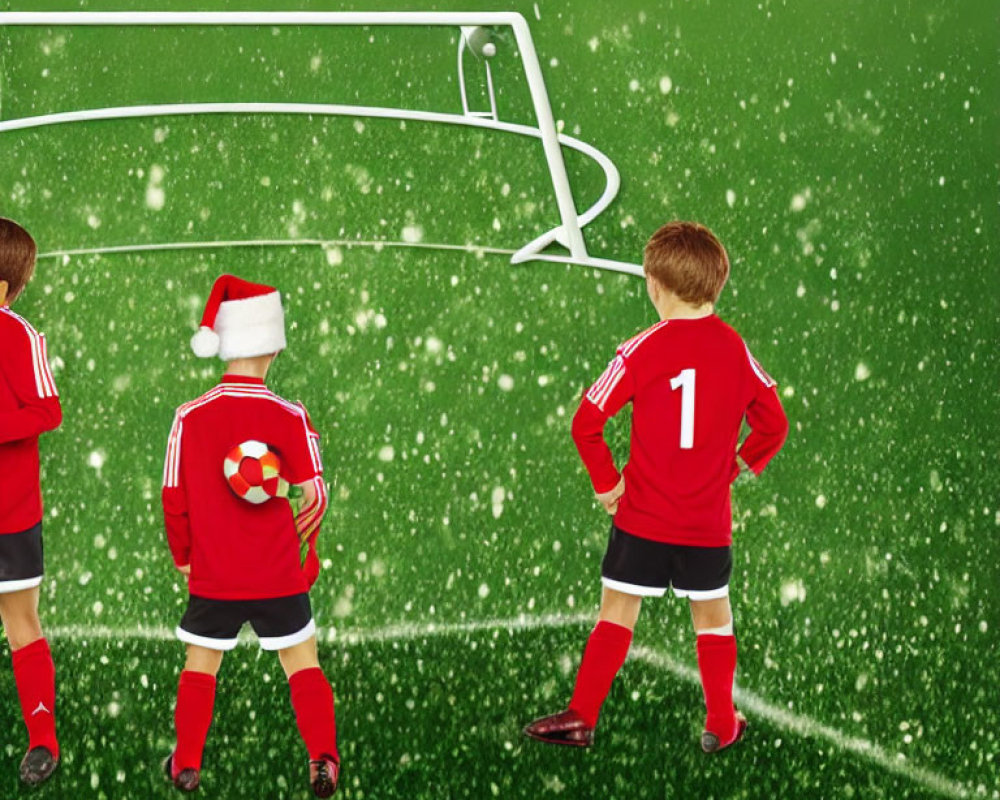 Children in red soccer uniforms on snowy green pitch with Santa hat.