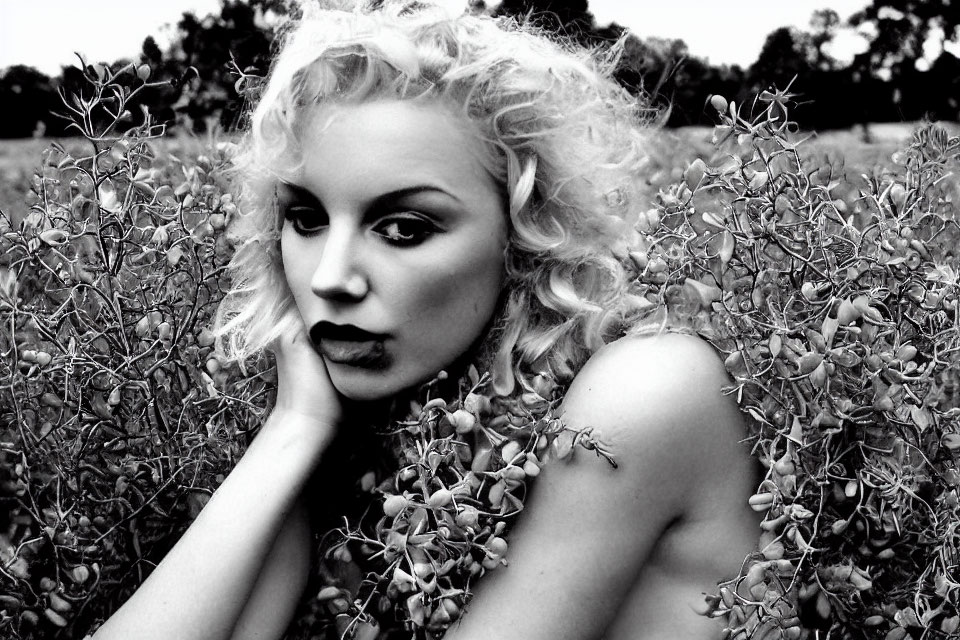 Monochrome portrait of woman with curly hair and bold lipstick in shrubbery