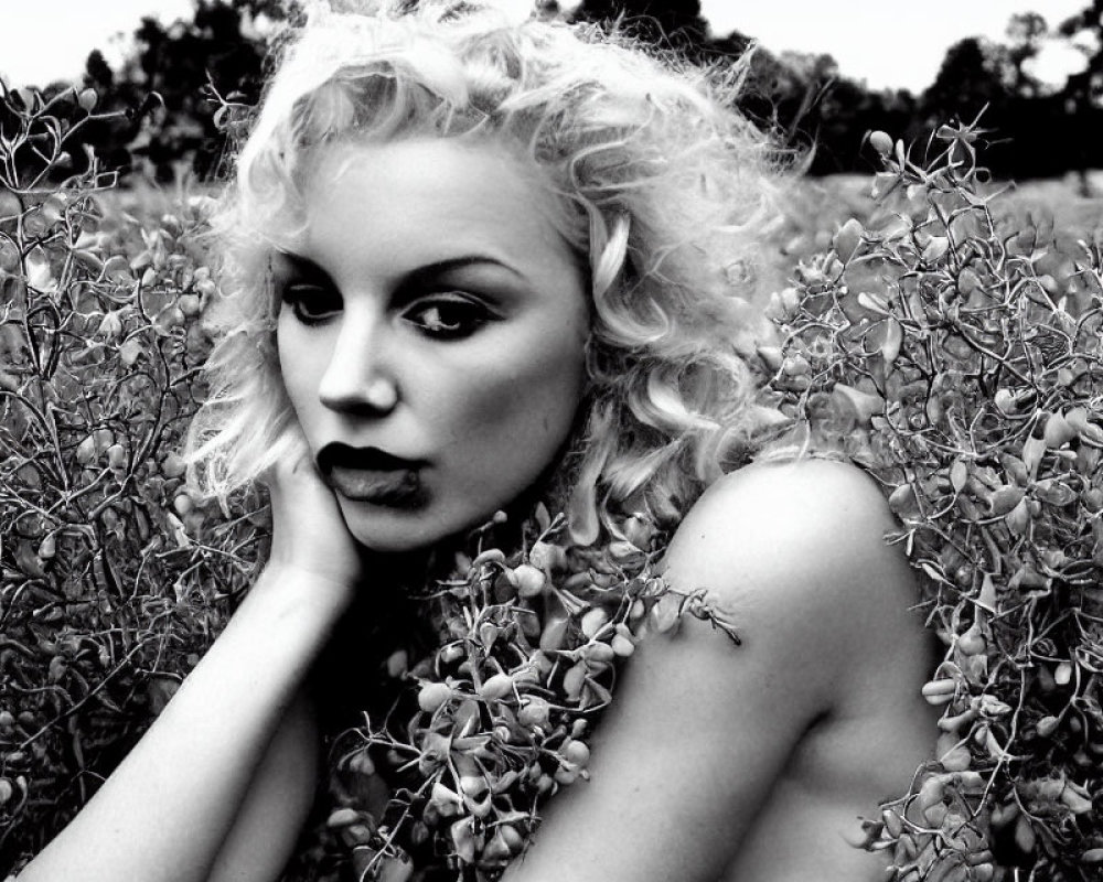 Monochrome portrait of woman with curly hair and bold lipstick in shrubbery