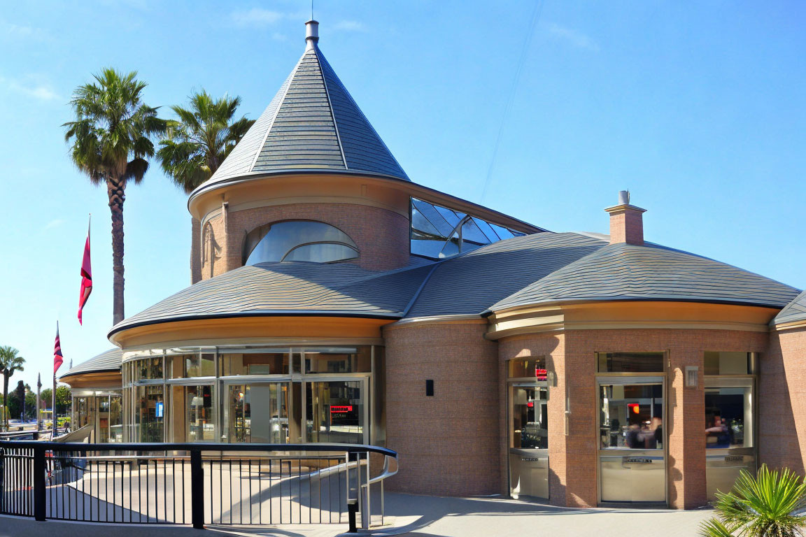 Modern building with conical roof, glass windows, and palm trees under clear sky