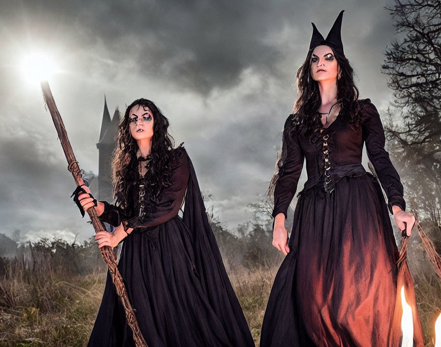 Two women in witch costumes with pointy hats in twilight forest.