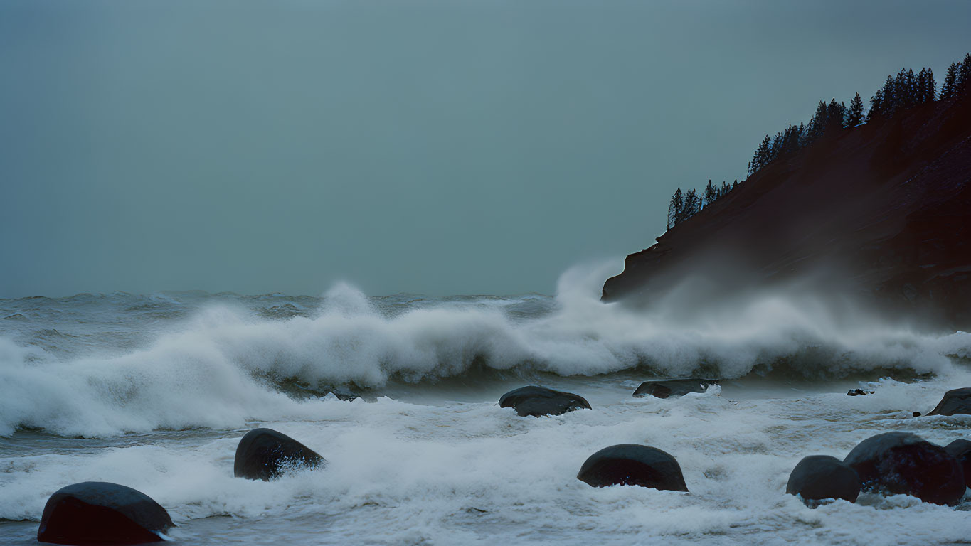 Rough sea with crashing waves on rocky shore and dark cliff under gloomy sky