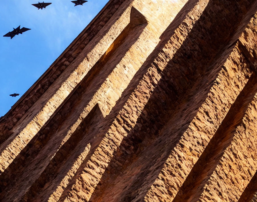 Stone arches textured pattern under clear blue sky with birds flying.