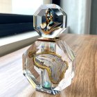 Crystal perfume bottle with gold and blue bust cap on wooden surface by window