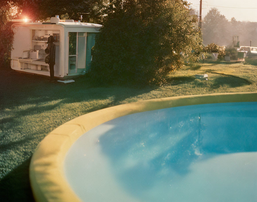 Tranquil backyard with above-ground pool and vintage trailer in sunlight