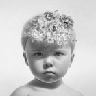 Monochrome portrait of a toddler with solemn expression and flower wreath