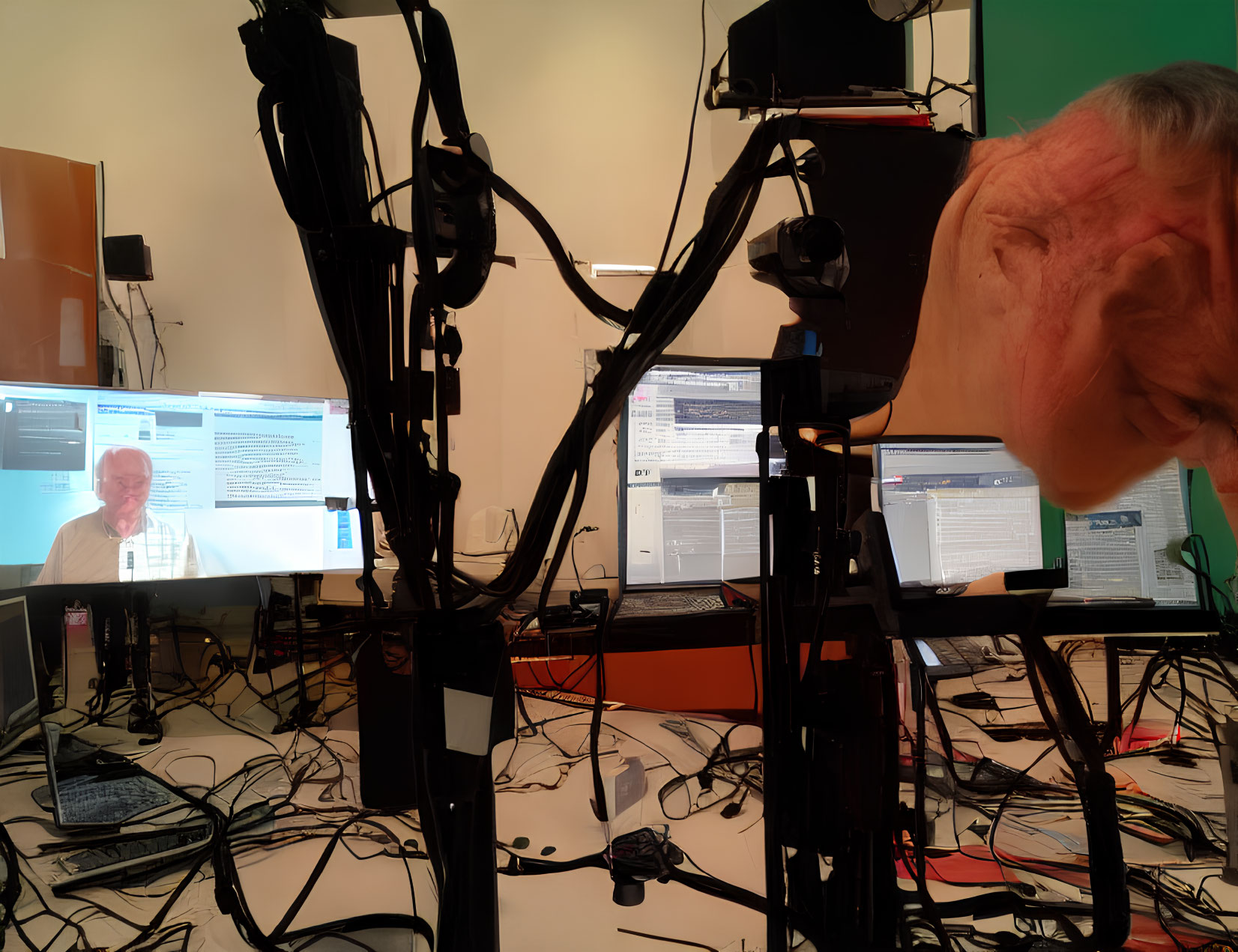 Broadcast set with cameras, screens, tangled wires, and man's face close-up.