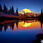 Snow-capped mountain sunrise reflected in serene lake amidst pine trees and rocks under twilight sky