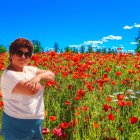 Woman in hat surrounded by red poppies and wildflowers under blue sky