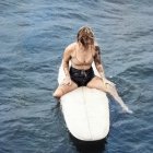 Woman in Blue Swimsuit Sitting on Surfboard in Ocean