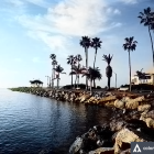 Tranquil beach scene with palm trees, blue water, red rocks, and green islets