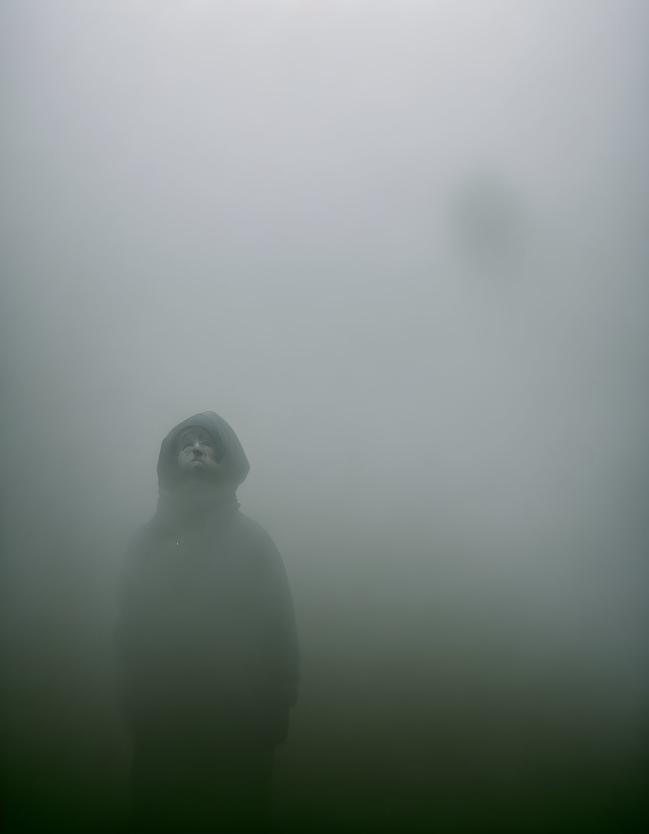 Hooded figure in dense fog with faint silhouette.