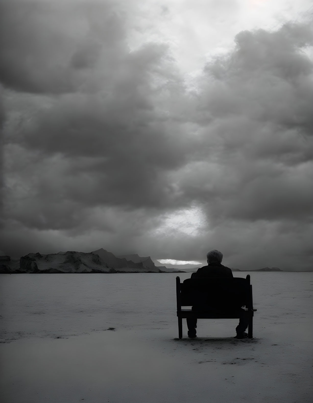 Person sitting on bench under dramatic sky with distant sunlight.