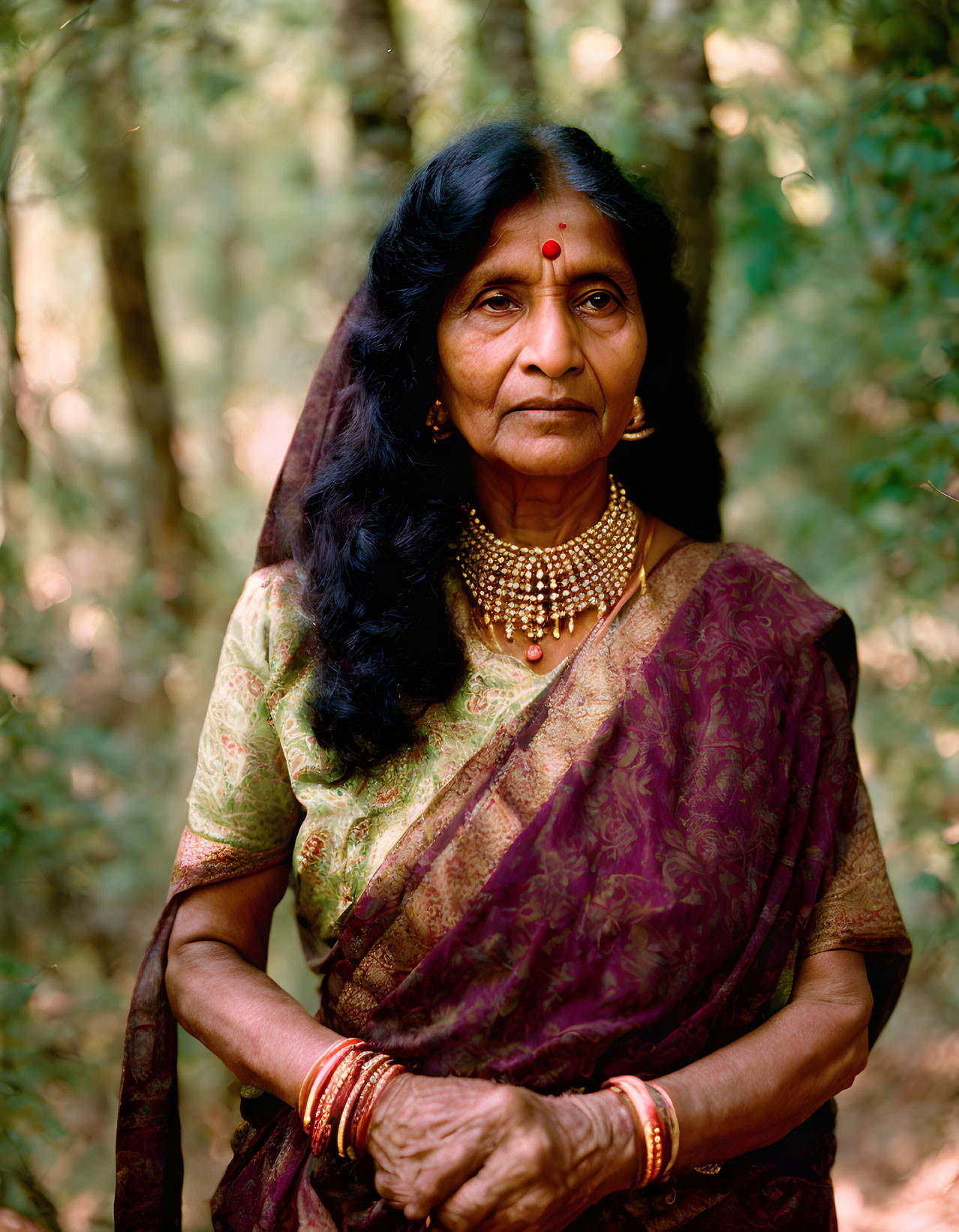 Elderly Indian woman in traditional attire with gold jewelry in forest