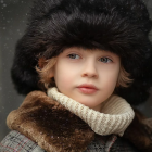 Child portrait with bright blue eyes in fur hat and coat on brown background